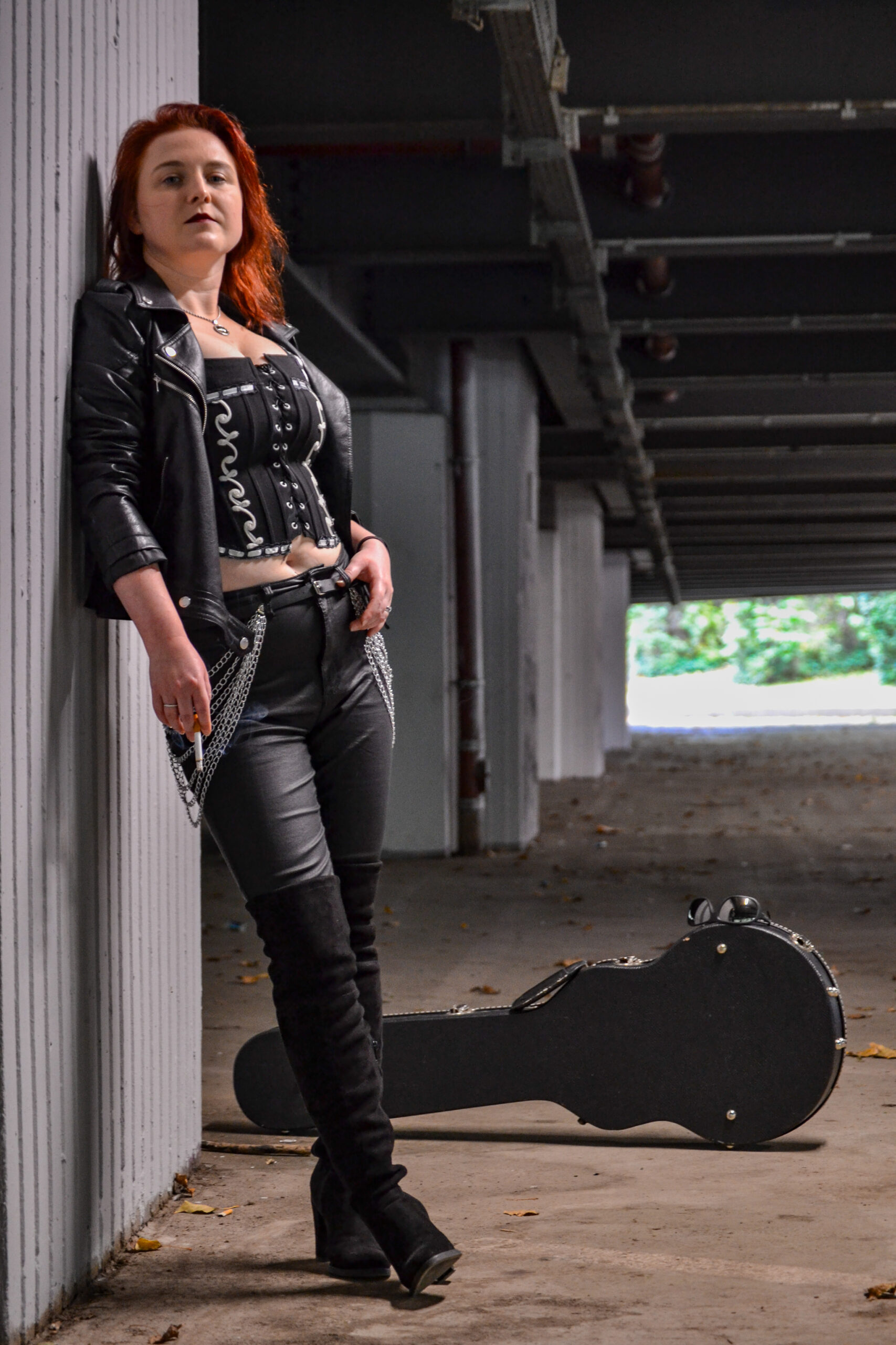 Sängerin lehnt an einer Wand mit Gitarrenkoffer im Hintergrund