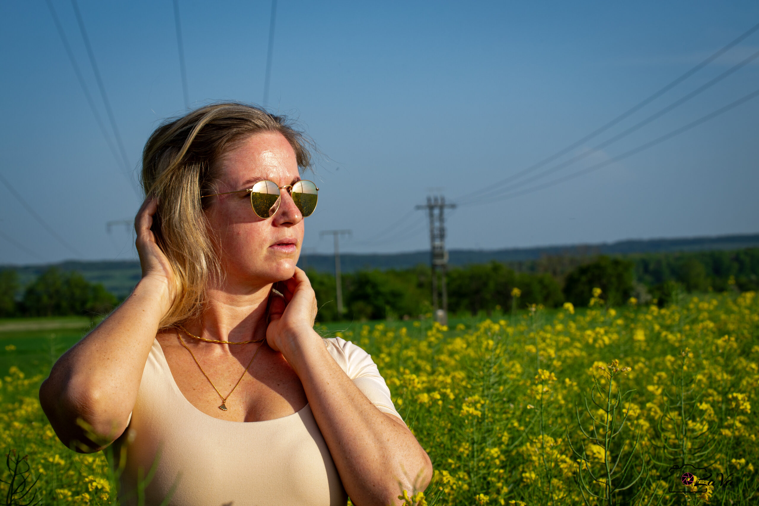 Frau blickt Richtung Sonne mit Sonnenbrille im Rapsfeld