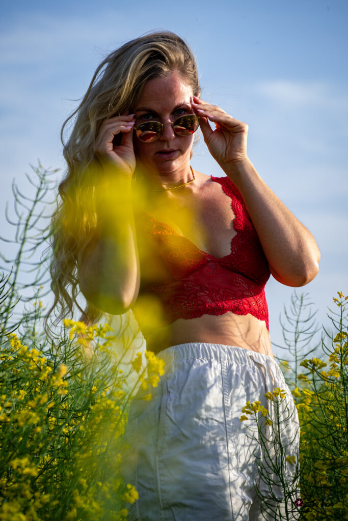 Blonde Frau blickt über Sonnenbrille in Kamera, Rapsfeld