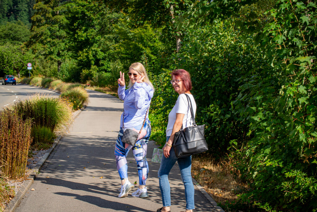 zwei Frauen spazieren im Wald und drehen sich nach hinten zur Kamera um